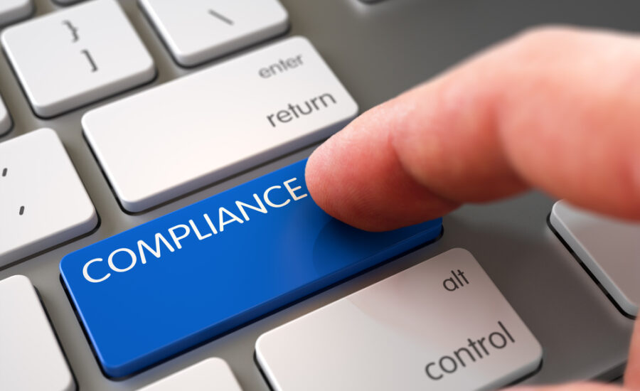 Finger pressing a blue 'COMPLIANCE' button on a grey keyboard, highlighting the importance of regulatory compliance in business practices and corporate governance.
